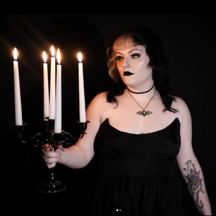 Woman in a black dress holding a candelabrum with lit candles against a dark background